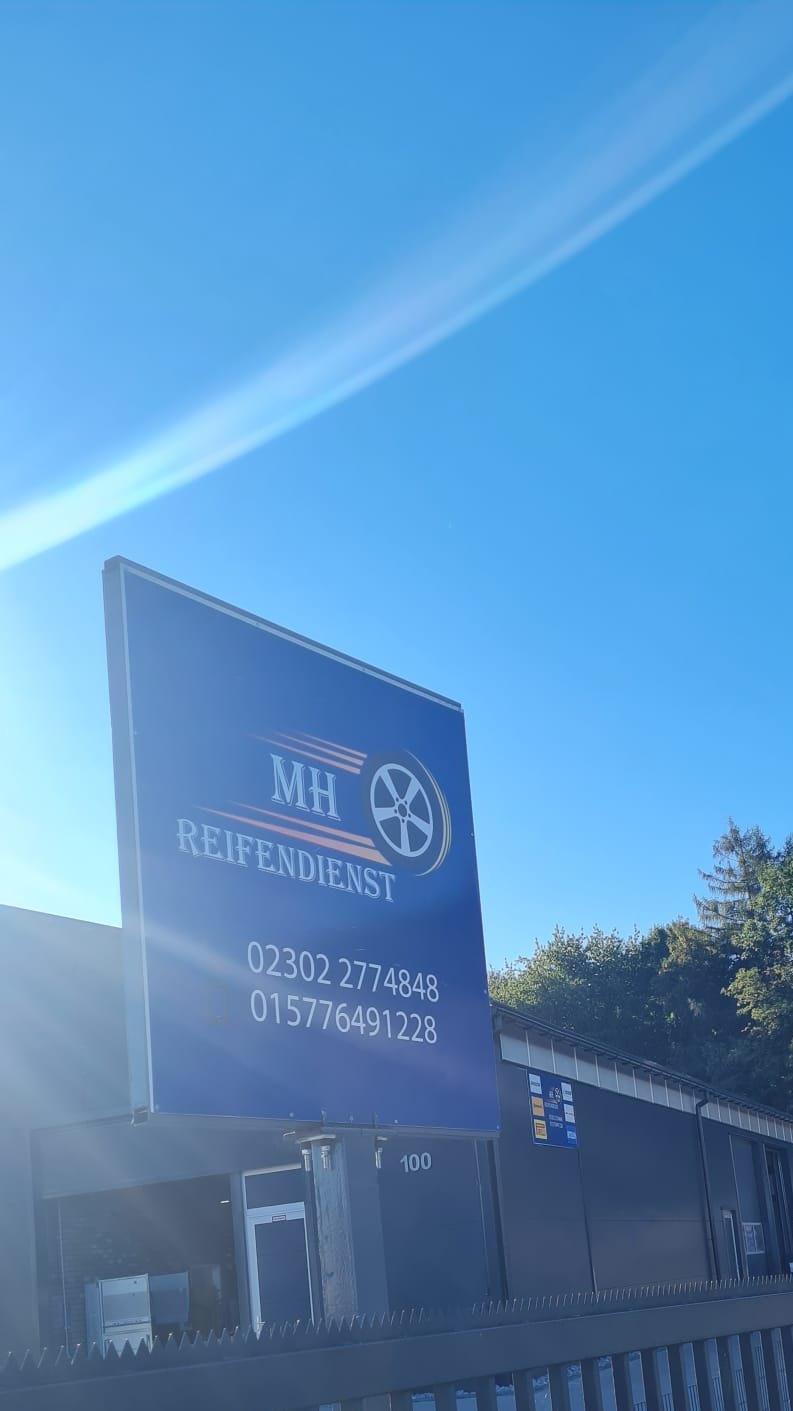 Blaues Schild von MH Reifendienst an der Einfahrt mit den Telefonnummern 02302 2774848 und 01577 6491228
